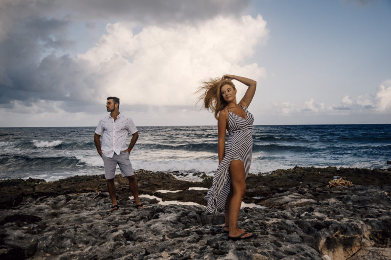 A man and woman standing on rocks near the ocean.
