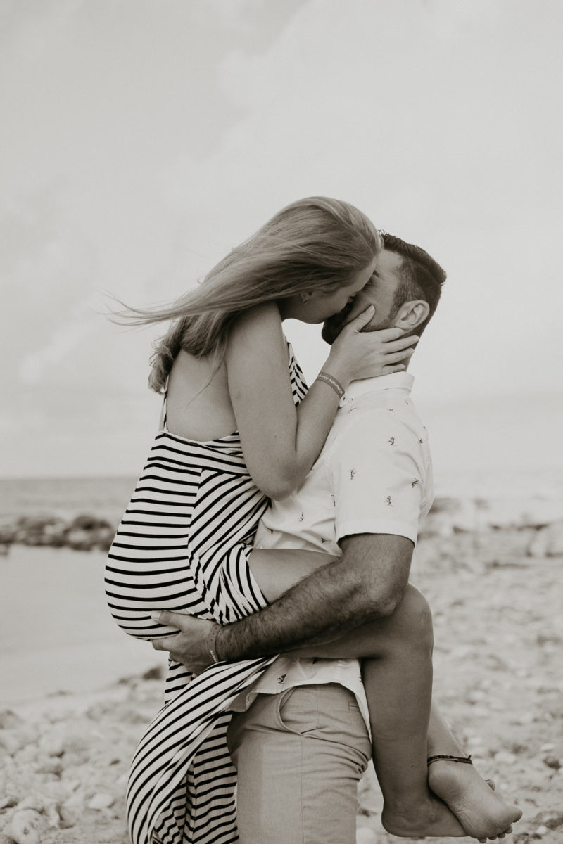 A black and white photo of a couple kissing on the beach captured by engagement photographer Beloveful